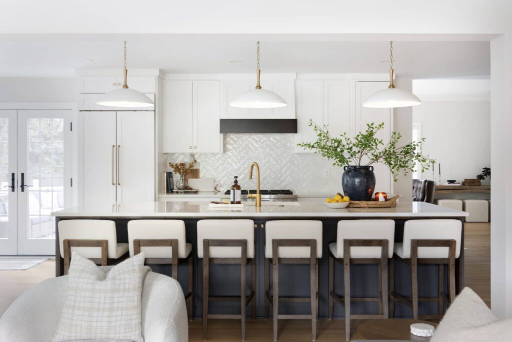 A spacious kitchen with a large center island featuring six barstools, pendant lighting, white cabinetry, and gold hardware, offering both style and function.
