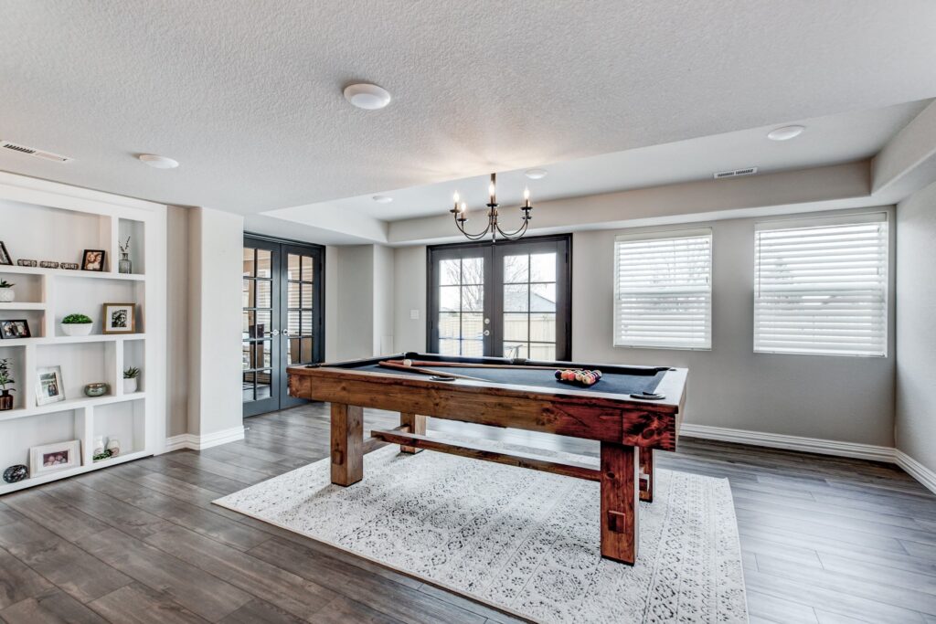 Spacious basement game room with pool table, French doors, and built-in shelving with display decor