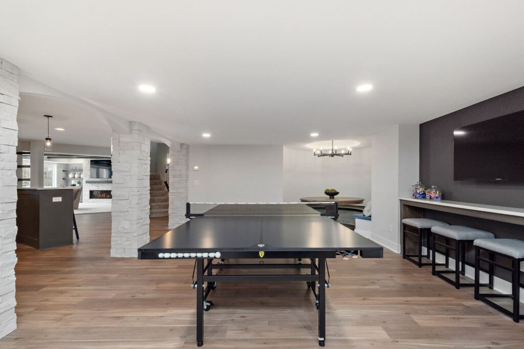 Spacious finished basement featuring a black ping pong table, stone columns, and bar seating area
