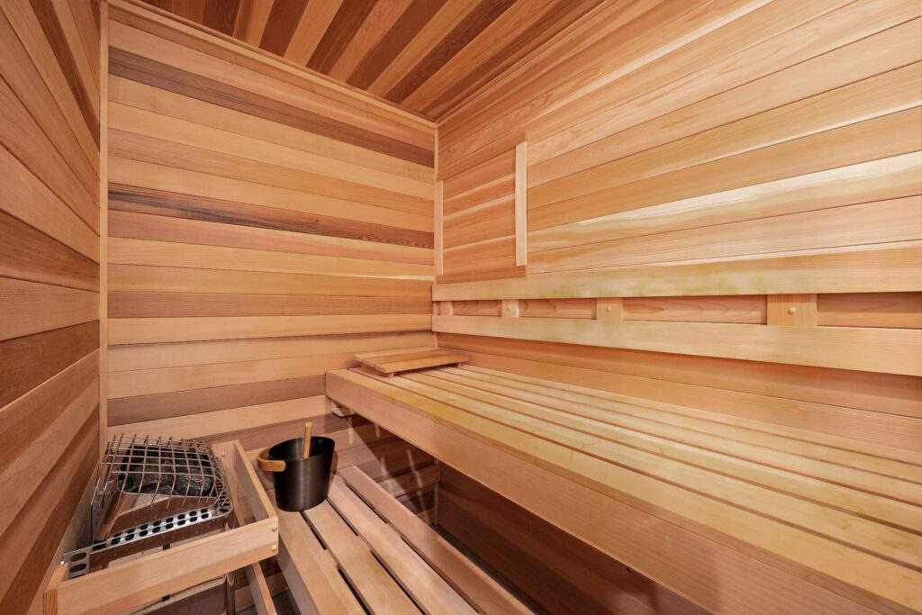 Wood-lined sauna with bench seating and a bucket near an electric heater
