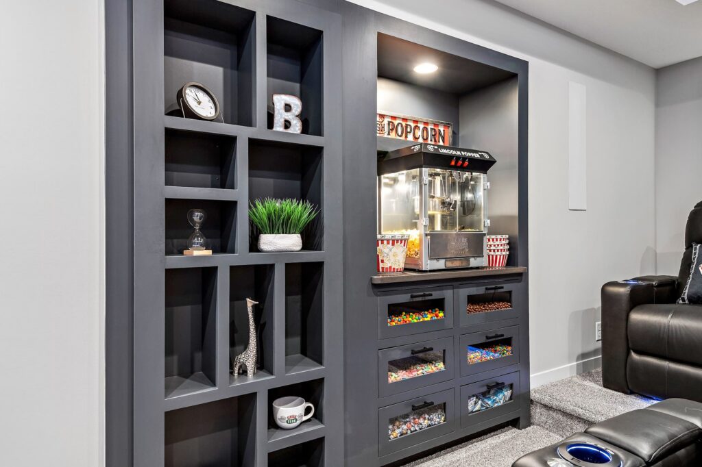 Built-in movie theater snack station with popcorn machine and candy drawers, framed by charcoal shelving