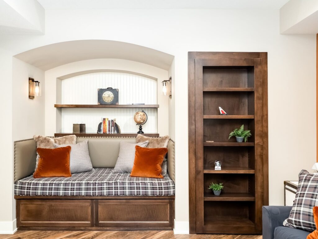 Cozy reading nook with built-in daybed, plaid cushion, rust velvet pillows, and adjacent wood bookshelf with decor