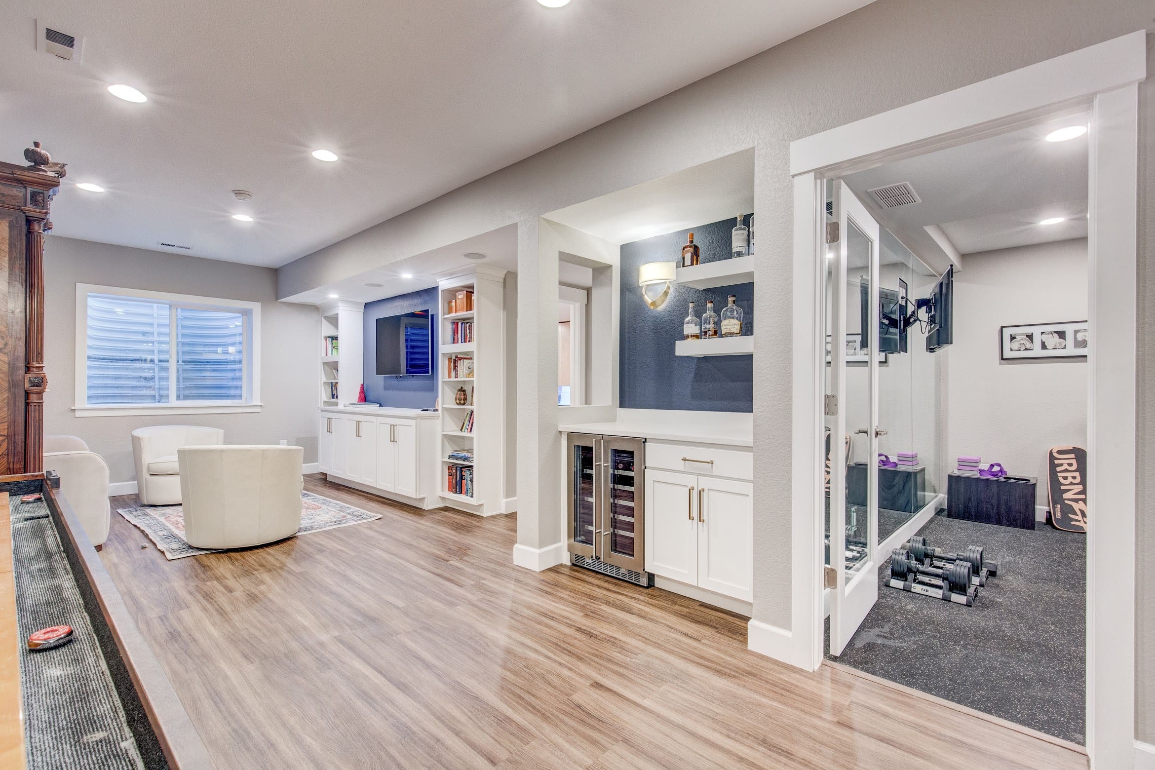 Sleek modern basement with home gym, wine fridge, built-in bookshelves, and luxury vinyl plank flooring