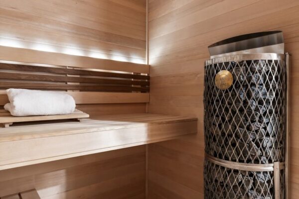 Custom sauna with wood slat seating and modern sauna heater on black hex tile flooring