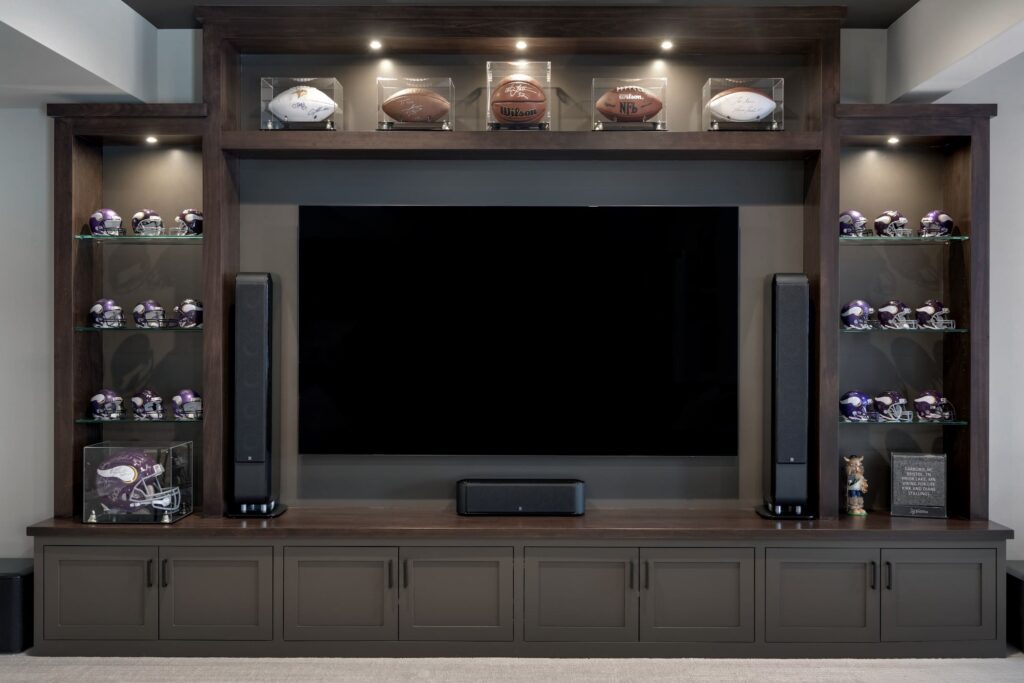 Home theater setup in basement with large dark wood entertainment center, glass shelves, and sports memorabilia display