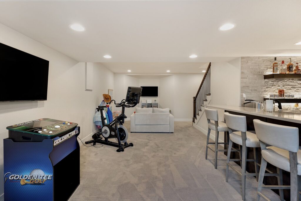 Multifunctional finished basement with fitness equipment, arcade machine, wet bar, and plush media area