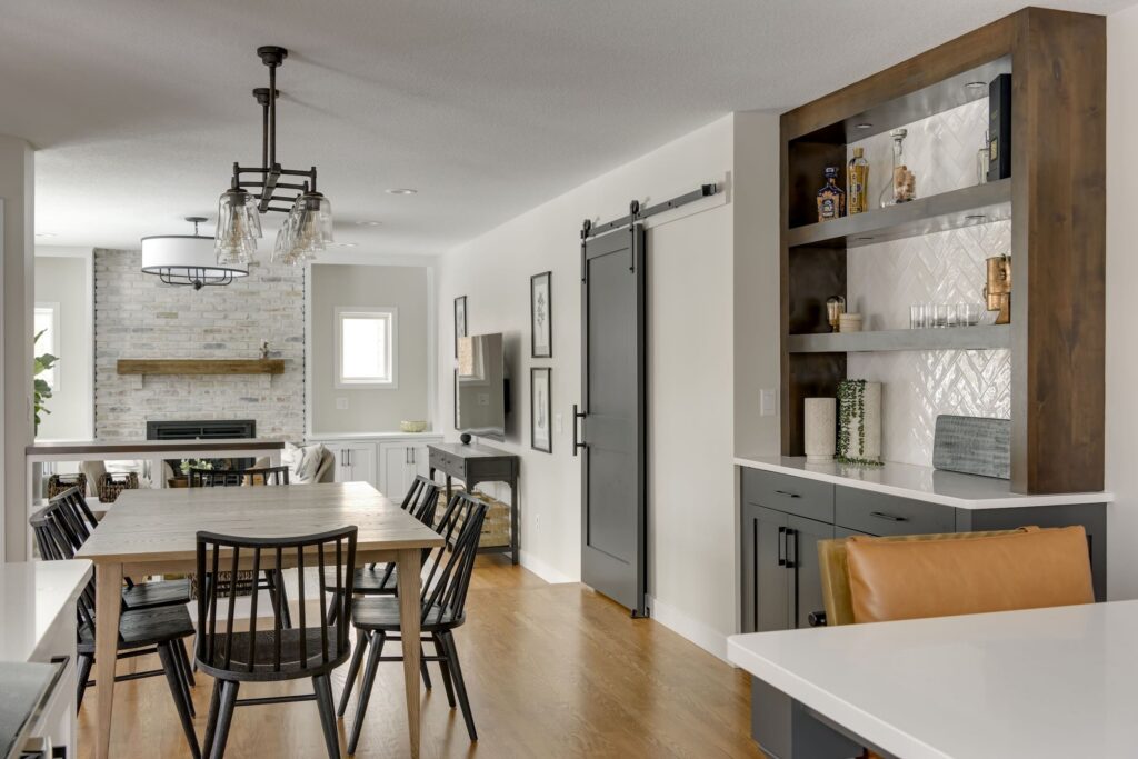 Modern open-concept basement with dining area, built-in bar shelving, and brick fireplace feature wall. apple valley basement remodeler