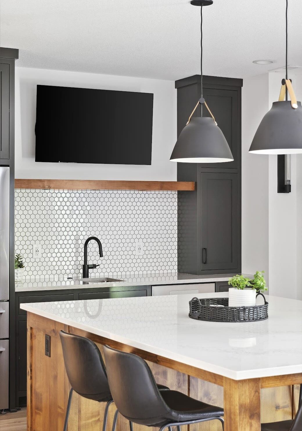 Modern basement kitchenette with white hex tile backsplash, matte black fixtures, and pendant lighting over island