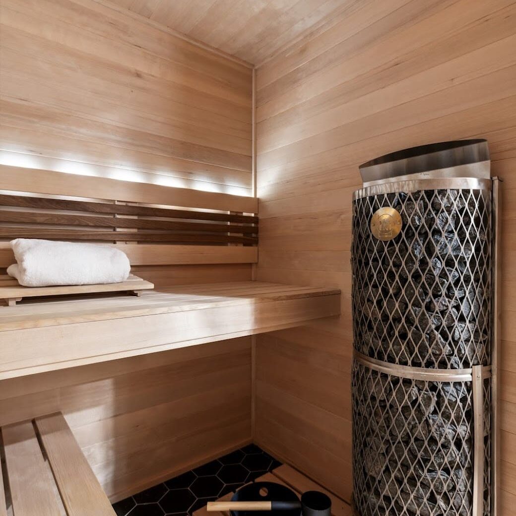 Custom sauna with wood slat seating and modern sauna heater on black hex tile flooring